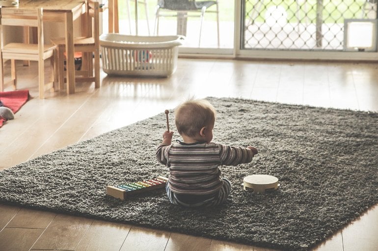 This shows a baby playing on a rug with a drum