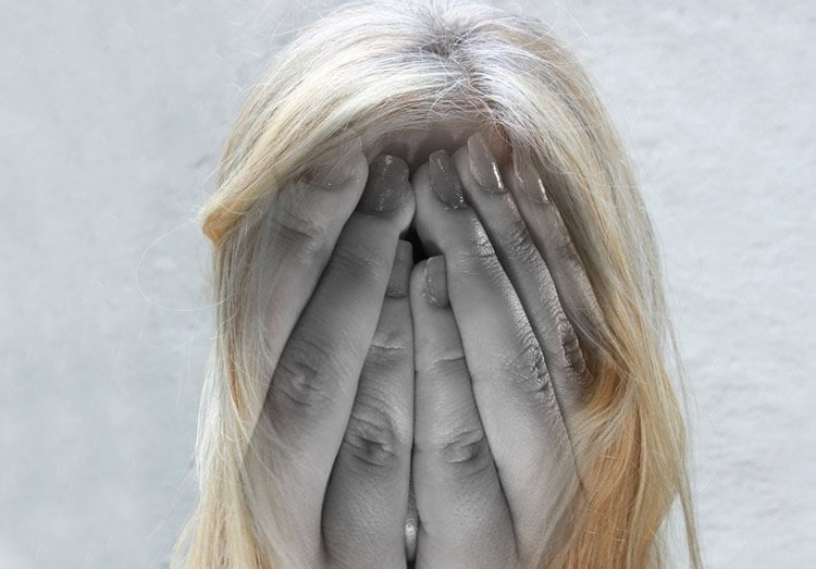 Image shows a woman holding her head in pain.