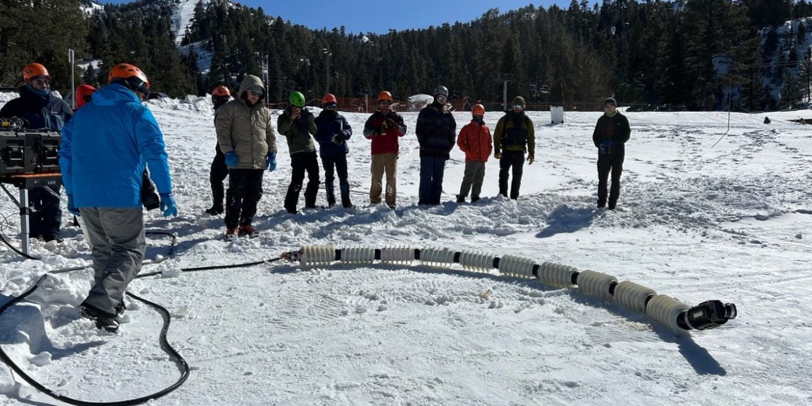 This shows the researchers in the snow with the EELS robot.