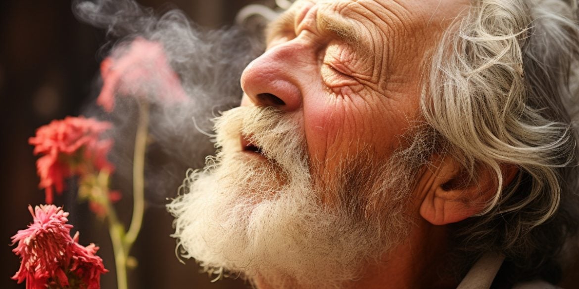 This shows an older man smelling a flower.