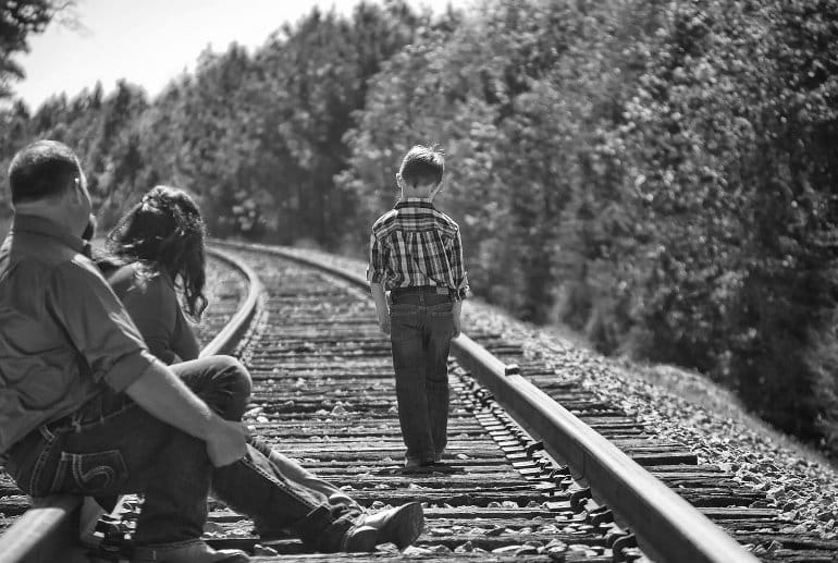 This shows a sad child walking away from his family down a train track
