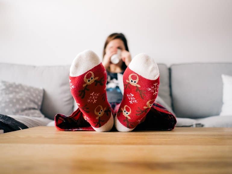 This shows a woman having a well earned break, resting her feet with santa socks on a table while relaxing with a hot drink
